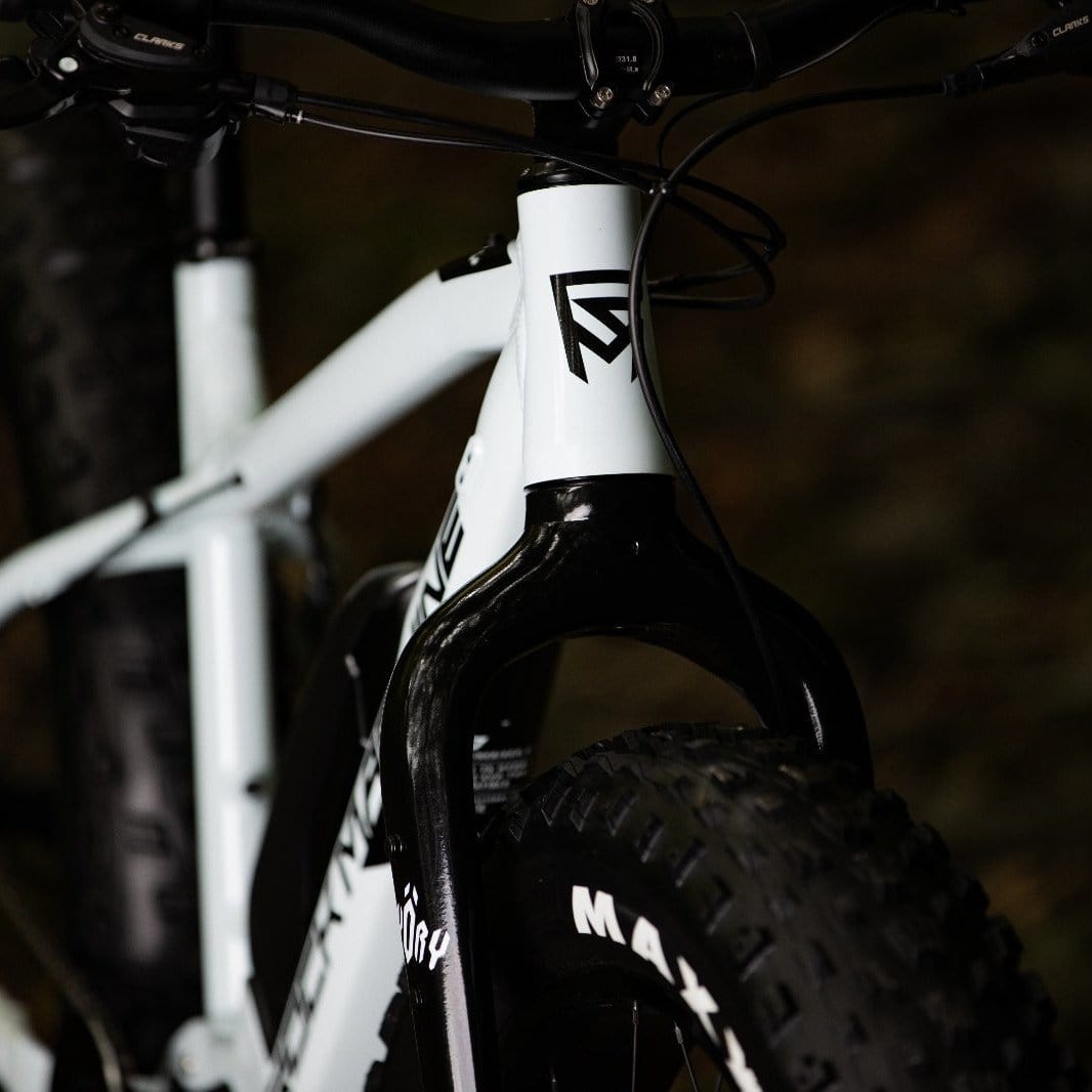 Lähikuva SÄHKÖPYÖRÄT.NETin Rock Machine Vyöry E50R:stä - valkoisesta e-fatbike-pyörästä, jossa on ohjaustanko, etuhaarukka, paksu Maxxis-rengas, geometrinen musta logo rungossa ja Shimano EP6 -moottori, joka parantaa suorituskykyä.