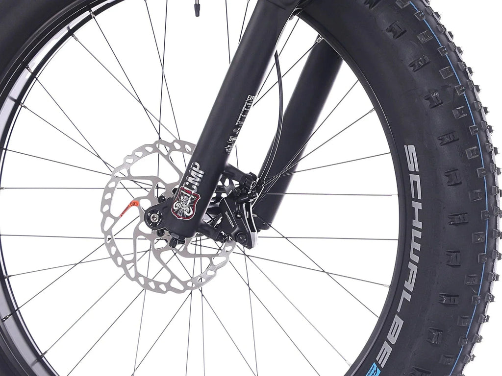 Lähikuva Rock Machine Vyöry E90 -etupyörästä, jossa on paksu Schwalbe-rengas, levyjarru-roottori ja musta jousitushaarukka, joka osoittaa SÄHKÖPYÖRÄT.NETin vankan rakenteen valkoista taustaa vasten.