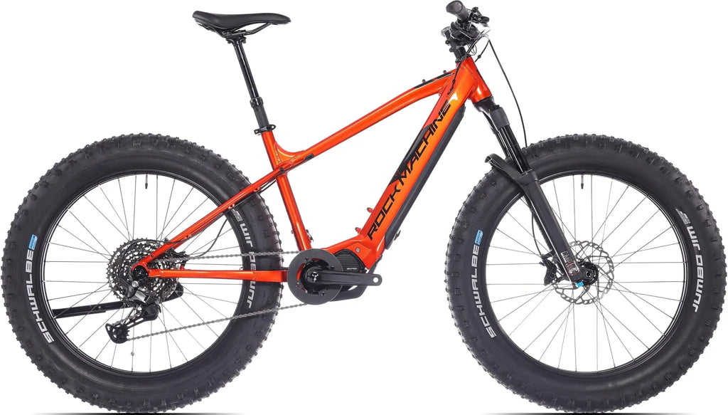 SÄHKÖPYÖRÄT.NETin Rock Machine Vyöry E90 on kirkkaan oranssi fatbike, jossa on mustat pyörät, istuin ja ohjaustanko. Siinä on Shimano EP6 -moottorituki ja erittäin leveät renkaat karkeaan maastoon.